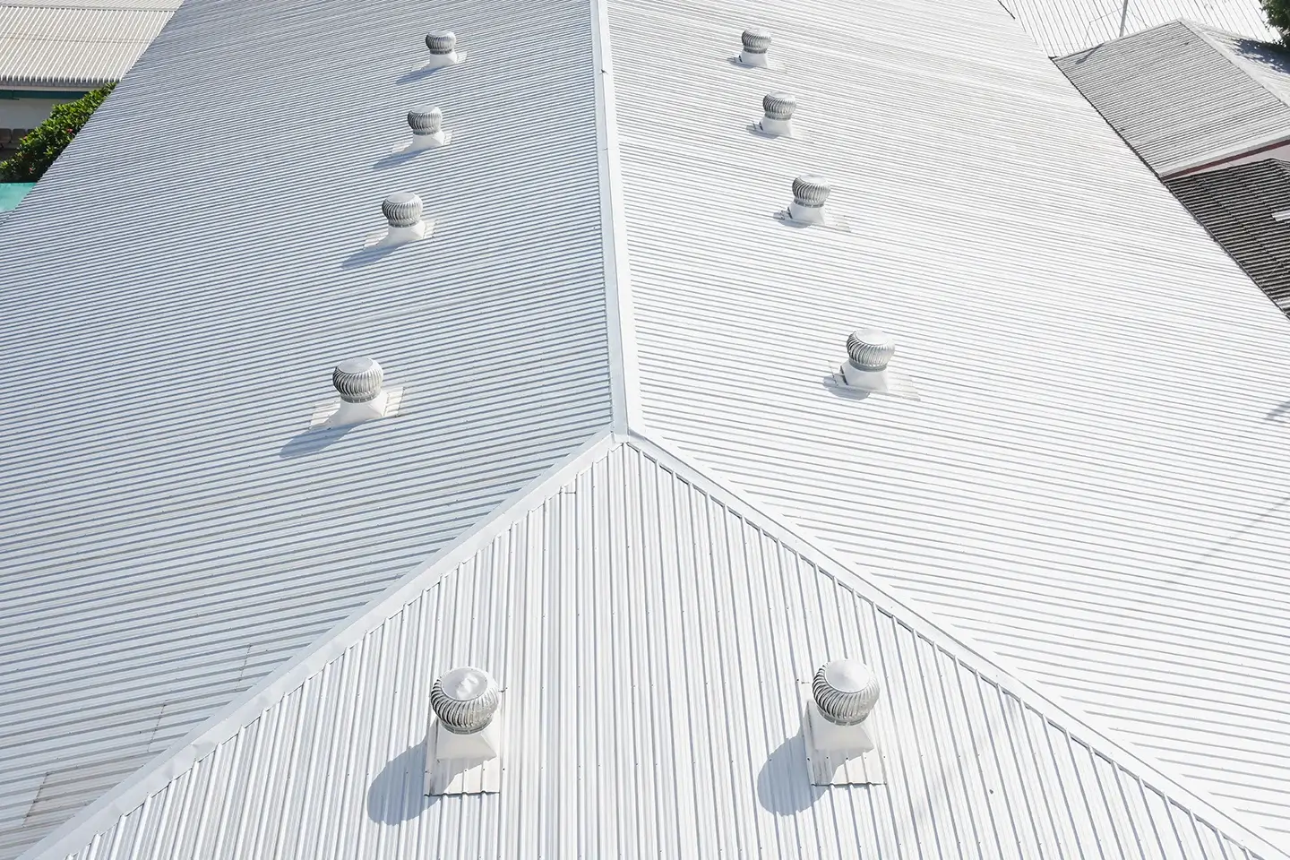 A bird's-eye view of a large, white, metal roof with multiple evenly spaced ventilation caps showcases the meticulous work of a skilled roofing contractor.