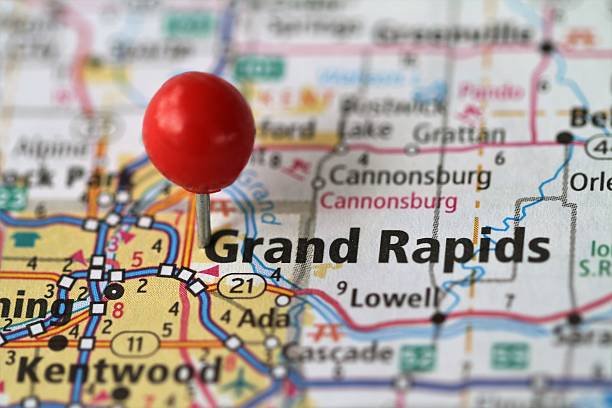 A close-up of a map with a red pushpin marking Grand Rapids, Michigan. Surrounding areas including Cannonsburg, Ada, and Lowell are visible. Major roads are highlighted on the map, perfect for a roofing contractor navigating to job sites in these regions.