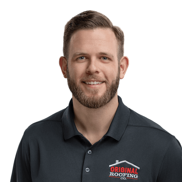 A bearded man smiles at the camera, wearing a black polo shirt with a logo that reads "Original Roofing Co." As an experienced roofer, he takes pride in delivering top-notch roofing services.
