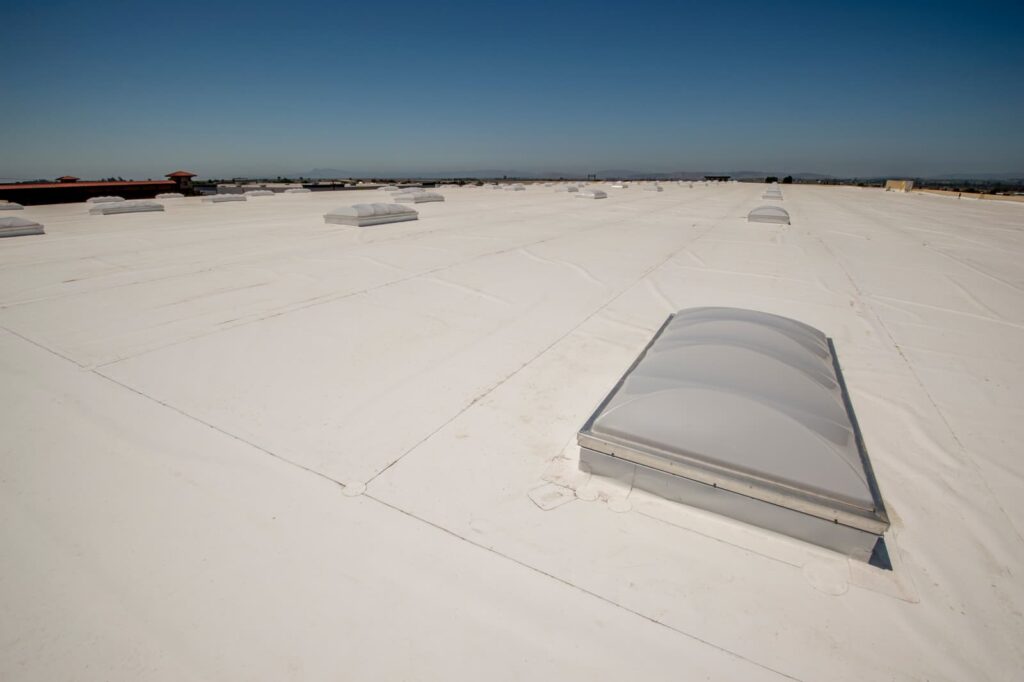 Flat white rooftop with multiple rectangular skylights evenly spaced across its surface, showcasing the precision of expert roofing services, all under a clear blue sky.