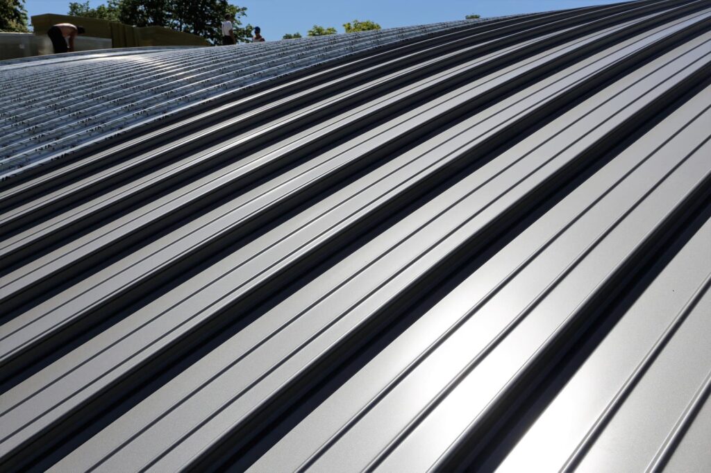 Close-up view of a corrugated metal roof reflecting sunlight, expertly installed by a local roofing company, with trees visible in the background.