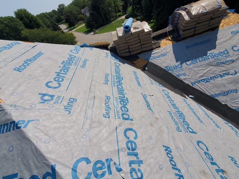Roofing Company in Crown Point, IN inspecting storm-worn shingles beside a residential gutter line
